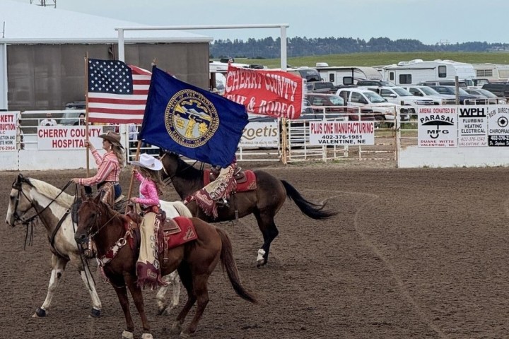 Riders on horseback carrying flags in a rodeo arena.