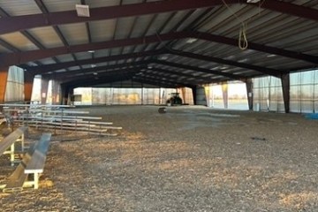Covered arena with metal bleachers, dirt floor, and tractor in the background.