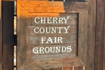 Wooden sign reads 'Cherry County Fair Grounds' with rustic texture.