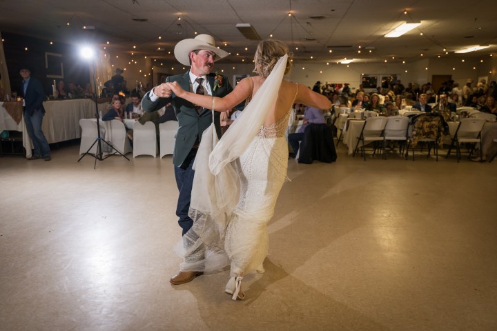 Bride and groom dancing in a brightly lit reception hall.
