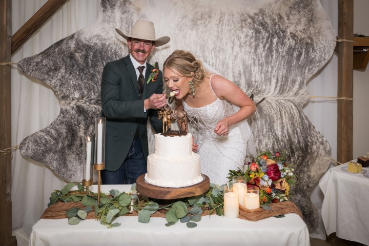 Bride and groom in cowboy attire cutting wedding cake indoors.