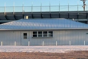 Metal building with doors labeled 'WOMEN' and 'MEN' under a clear sky.